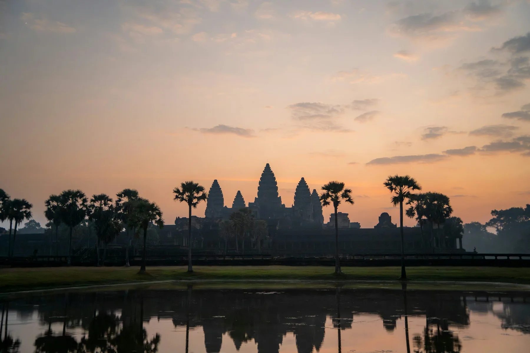 Angkor Wat and palm trees reflected in the water at dawn